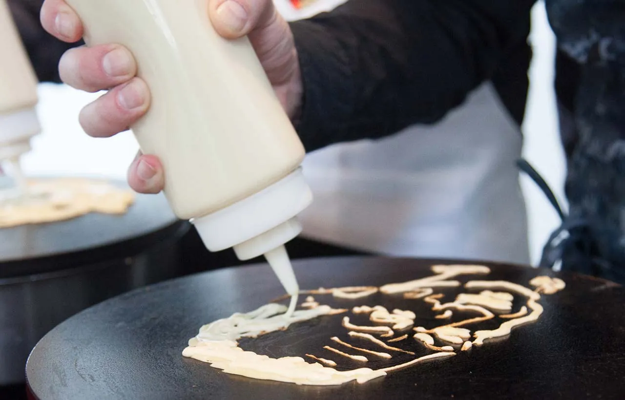 Pancake Portrait entsteht: Pfannkuchenteig wird aus einer Flasche als Porträt auf die heiße Platte gezeichnet