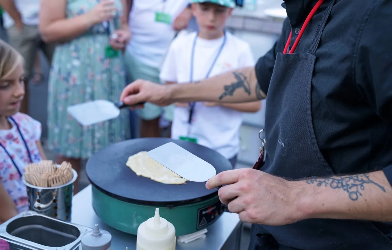 Künstler wendet einen Pfannkuchen auf der Platte, Kinder schauen zu
